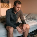 Man in running clothes examining his Oura Ring on the edge of his bed in morning light.