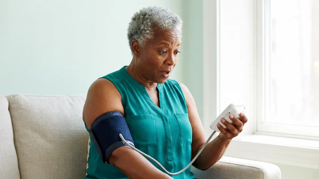 Surprised woman in her 60s reading a home monitor while a too-small blood pressure cuff strains on her arm