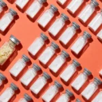 Rows of plain BPC-157 vials on coral, one with yellowed powder, a crooked cap and cracked glass